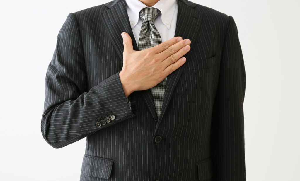 胸に手を当てるスーツ姿の男性